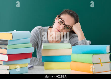Young Tired Woman Sitting With Stack Of Books In Classroom Stock Photo