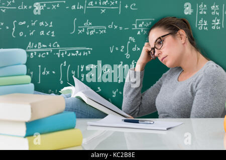 Young Woman Reading Books At Desk In Classroom Stock Photo