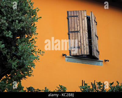 window with half-open wooden shutters set in ochre painted wall of typical hillside house in Tuscany, Italy Stock Photo