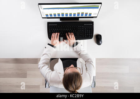 High Angle View Of Businessperson Analyzing Graph On Computer At Desk Stock Photo