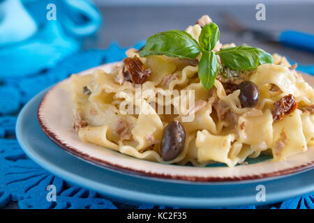 Pasta with olives, tuna, sun dried tomatoes and olive oil in a white and blue plate on a blue cloth. Mediterranean lifestyle. Healthy eating concept. Stock Photo