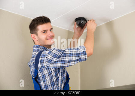 Young Male Technician Installing Surveillance Camera On Ceiling Stock Photo