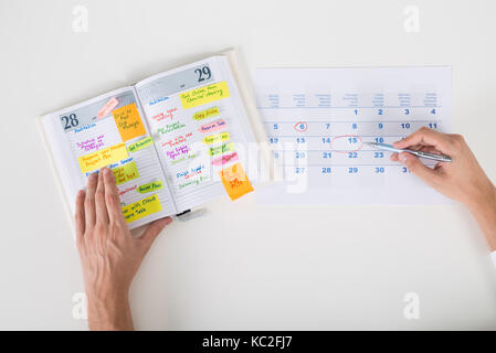 Close-up Of Person Hands Highlighting Date On Calendar With Diary At Desk Stock Photo