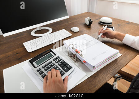 Close-up Of Businessman Checking Invoice With Calculator At Desk Stock Photo