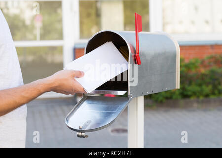 Close-up Of Person Putting Stack Of Letters In Mailbox Stock Photo