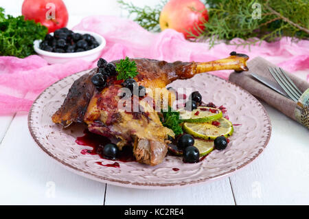 Baked goose leg in berry sauce on a ceramic plate on a white wooden background. Stock Photo