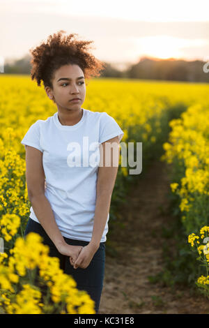 Beautiful mixed race African American girl teenager female young woman outside on a path in a field of yellow flowers looking scared sad depressed or  Stock Photo