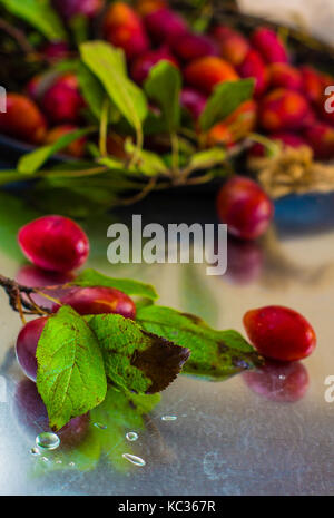 Fresh organic plums with leaves on old rustic wooden table Stock Photo