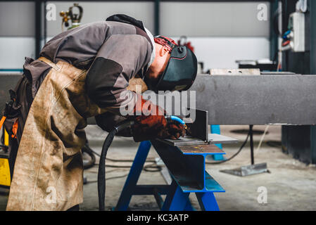 Industrial Welder With Torch and Protective Helmet in big hall welding metal profiles Stock Photo