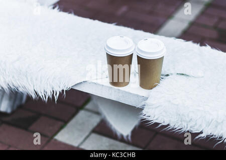 Two cup takeaway hot drink on bench seat covered with natural wool for warmth in winter Stock Photo