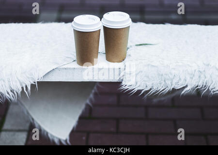 Two cup takeaway hot drink on bench seat covered with natural wool for warmth in winter Stock Photo