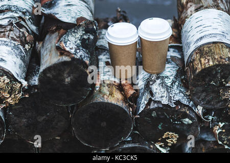 Two carton paper cups  coffe to go on stack of logs for firewood Stock Photo