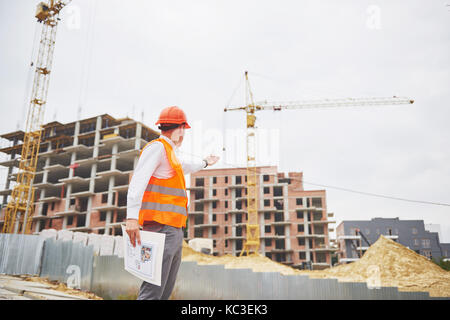 architecture and home renovation concept - man in helmet and gloves with blueprint in factory Stock Photo