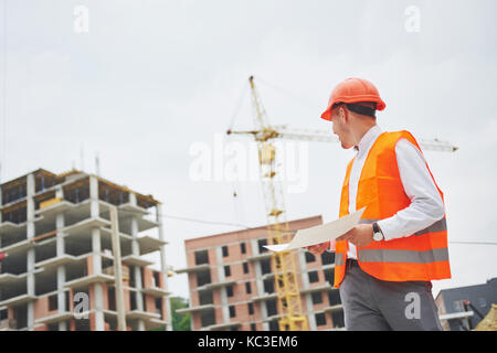architecture and home renovation concept - man in helmet and gloves with blueprint in factory Stock Photo