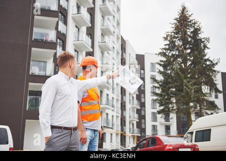 construction, architecture, business, teamwork and people concept - happy architects with blueprint at building site Stock Photo