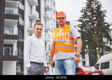 construction, architecture, business, teamwork and people concept - happy architects with blueprint at building site Stock Photo