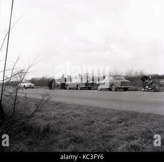 1964, historical, police officers in a Jaguar police car, a poilce Austin Cambridge car and a police motorcycle, investigate a small burnt-out van parked in a lay-by beside a country road, England, UK. Stock Photo