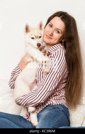 Happy beautiful woman hugging puppy husky. girl sitting on a sofa with a dog Stock Photo