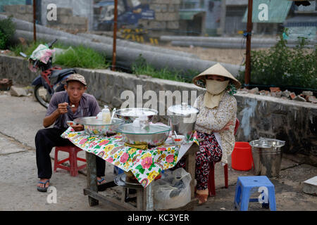 The old man is sitting in front of a woman's booth on the street. Stock Photo