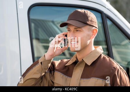 Portrait of smiling delivery man using mobile phone against truck Stock Photo