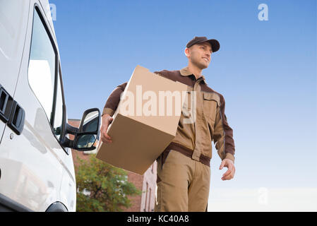 Low angle portrait of young delivery man carrying cardboard box against sky Stock Photo