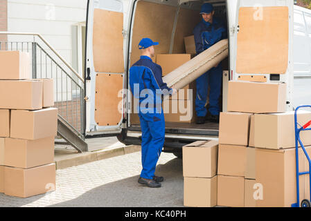 Young male movers unloading rolled up rug from truck on street Stock Photo