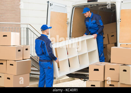 Young male movers unloading furniture and cardboard boxes from truck on street Stock Photo