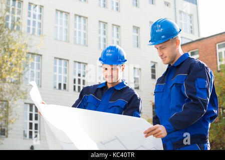 Young male architects analyzing blueprint together outdoors Stock Photo