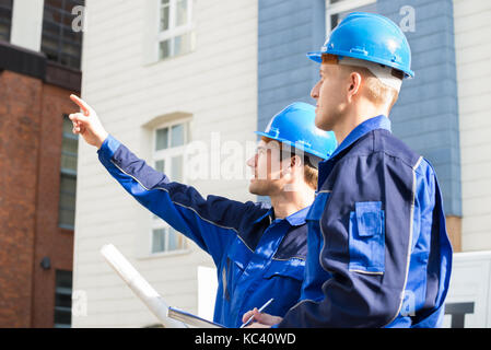 Young male architect showing something to colleague while analyzing blueprint outdoors Stock Photo