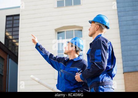 Male architect showing something to colleague while holding blueprint outdoors Stock Photo