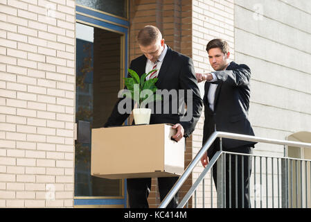 Side view of businessman firing employee carrying box with belongings outside office Stock Photo