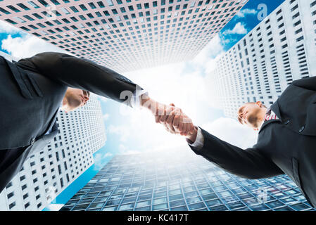 Directly below shot of businessmen shaking hands against office buildings Stock Photo
