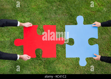 Cropped image of businessmen joining jigsaw pieces over grassy field Stock Photo