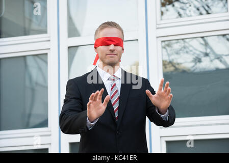 Blindfolded young businessman gesturing while standing against window outdoors Stock Photo
