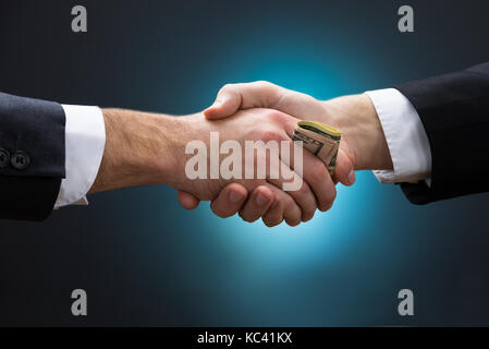 Cropped image of businessman shaking hands while giving bribe to partner against blue background Stock Photo