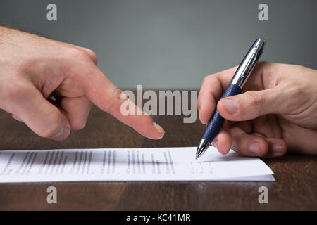 Cropped image of businessman pointing partner to sign agreement at desk Stock Photo