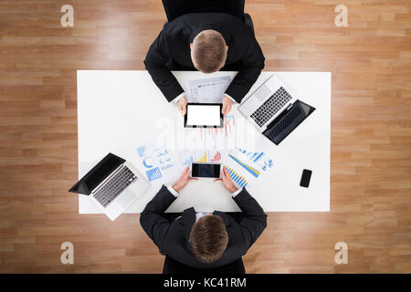 Directly above shot of businessmen using technologies with financial charts on table Stock Photo