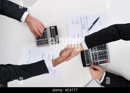 Directly above shot of businessmen shaking hands while calculating finance at desk Stock Photo