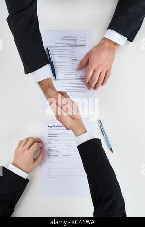 Cropped image of businessman shaking hands with male candidate at desk Stock Photo