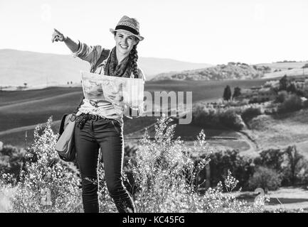 Discovering magical views of Tuscany. happy young woman hiker with bag on Tuscany hike holding map and pointing Stock Photo