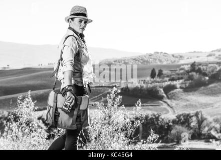 Discovering magical views of Tuscany. Portrait of active woman hiker with bag enjoying Tuscany view with vintage photo camera Stock Photo