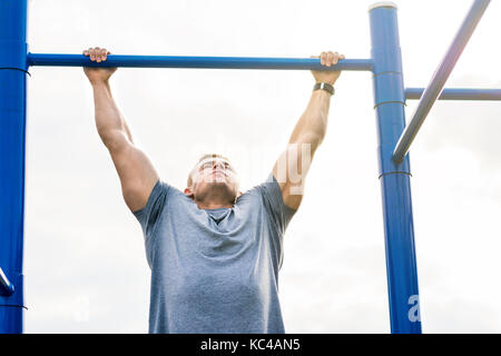 Masculine man doing pull ups on street workout outdoors Stock Photo