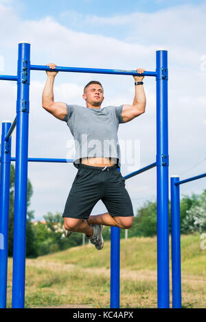 Masculine man doing pull ups on street workout outdoors Stock Photo