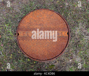 Old rusty electrical manhole cover in a grassy field. Stock Photo