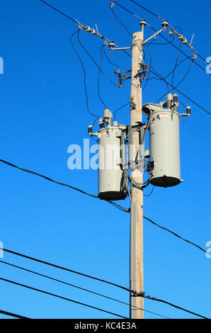 Two electrical transformers on a pole with many wires and cables with a deep blue sky background. Stock Photo