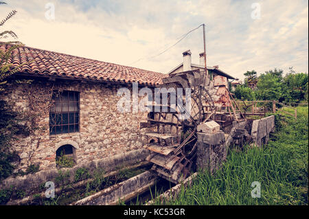 Old water mill with iron water wheel. Photo in vintage style. Stock Photo