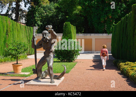 Formal garden, rear view of a solo woman traveler walking past a modernist statue of Hercules in the Jardin de las Hesperides, Valencia, Spain Stock Photo