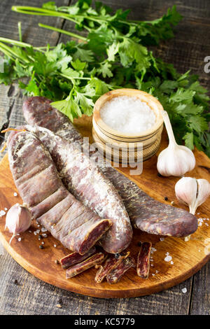 Beef jerky smoked sausage sudzhuk with spices and garlic is served on a cutting board. Stock Photo