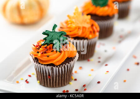 Autumn delicious cupcakes decorated with orange frosting, colorful sprinkles and maple leaves Stock Photo