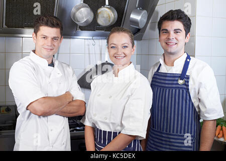 Portrait Of Chef And Staff Standing By Cooker In Kitchen Stock Photo